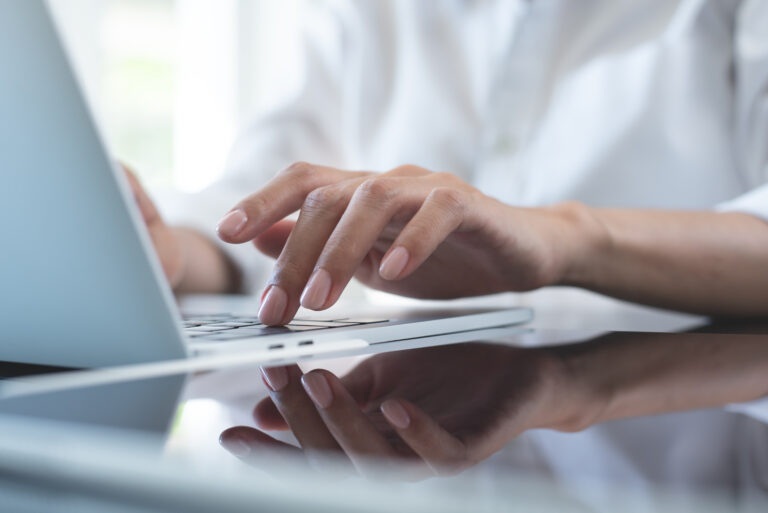 Close up of business woman hand typing on laptop computer keyboard with reflection on digital tablet on office table, online working, surfing the internet, distant job, remote work concept
